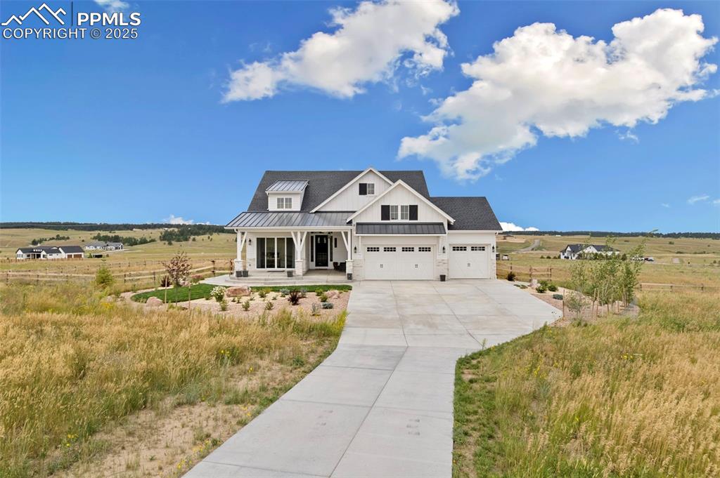 Modern farmhouse style home featuring a standing seam roof, a porch, a metal roof, driveway, and a view of rural / pastoral area