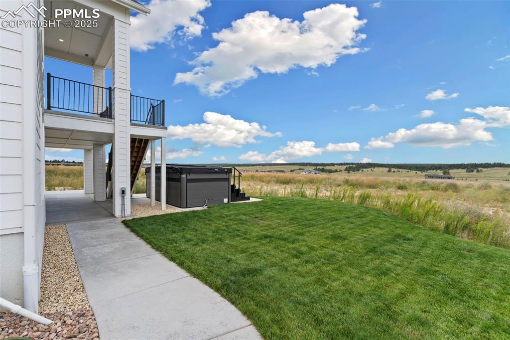 View of grassy yard with a patio, a hot tub, and a view of countryside
