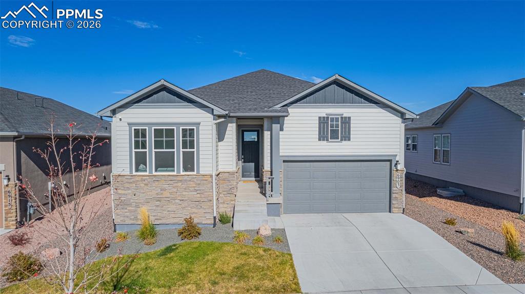 View of front of house featuring stone siding, a garage, concrete driveway, board and batten siding, and roof with shingles