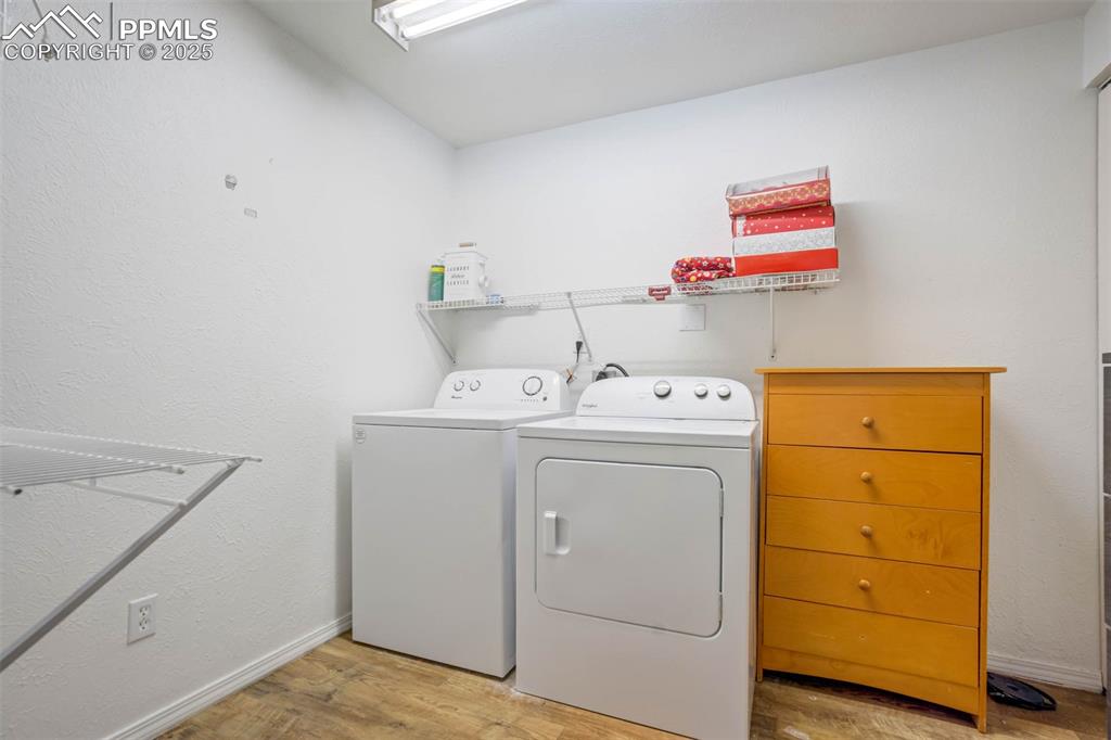 Laundry area featuring a textured wall, light wood-type flooring, and washer and clothes dryer