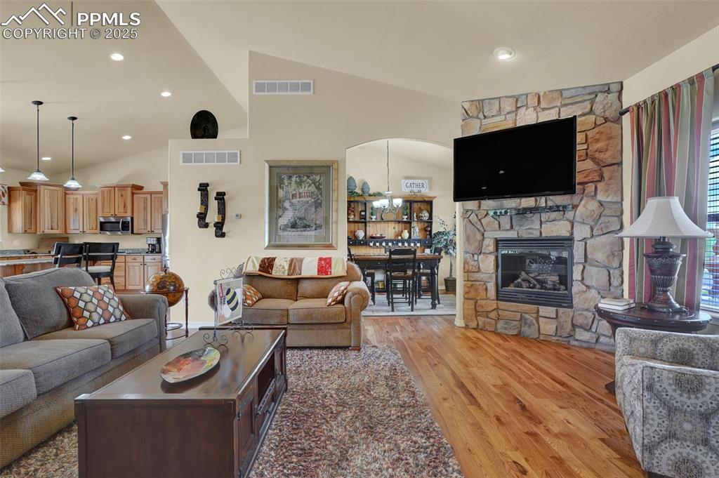 Living room featuring a stone fireplace, visible vents, vaulted ceiling, and light wood-style flooring