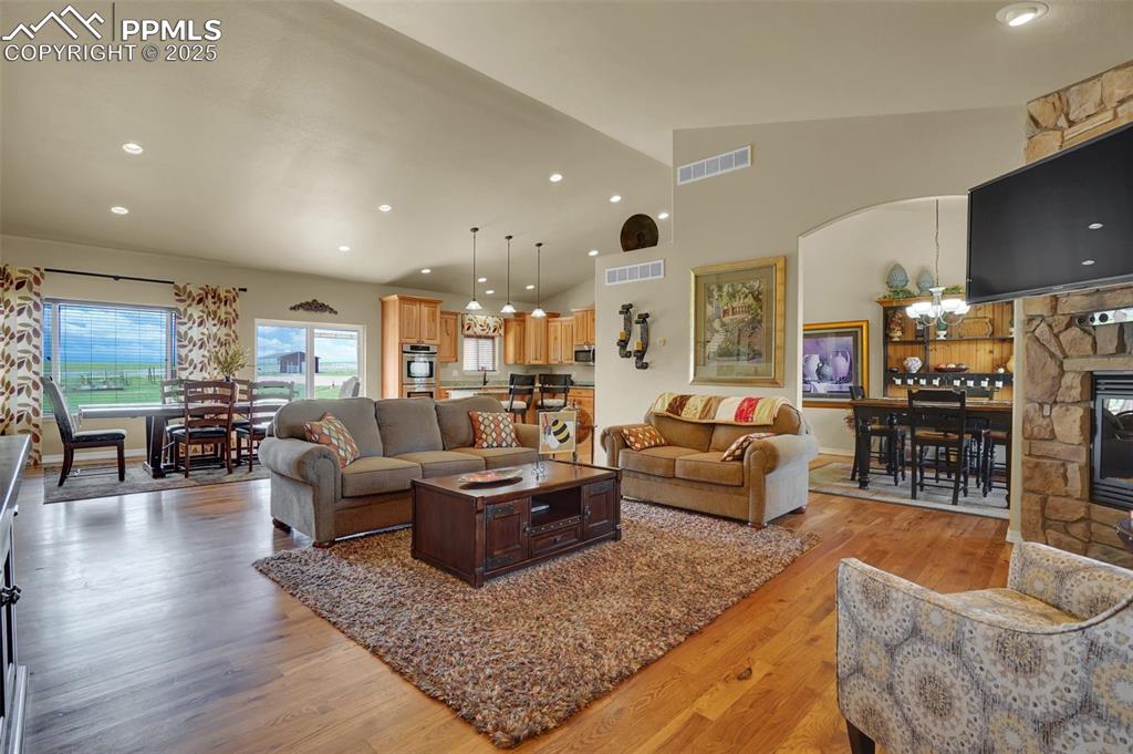 Living area featuring light wood-style floors, a stone fireplace, visible vents, and high vaulted ceiling