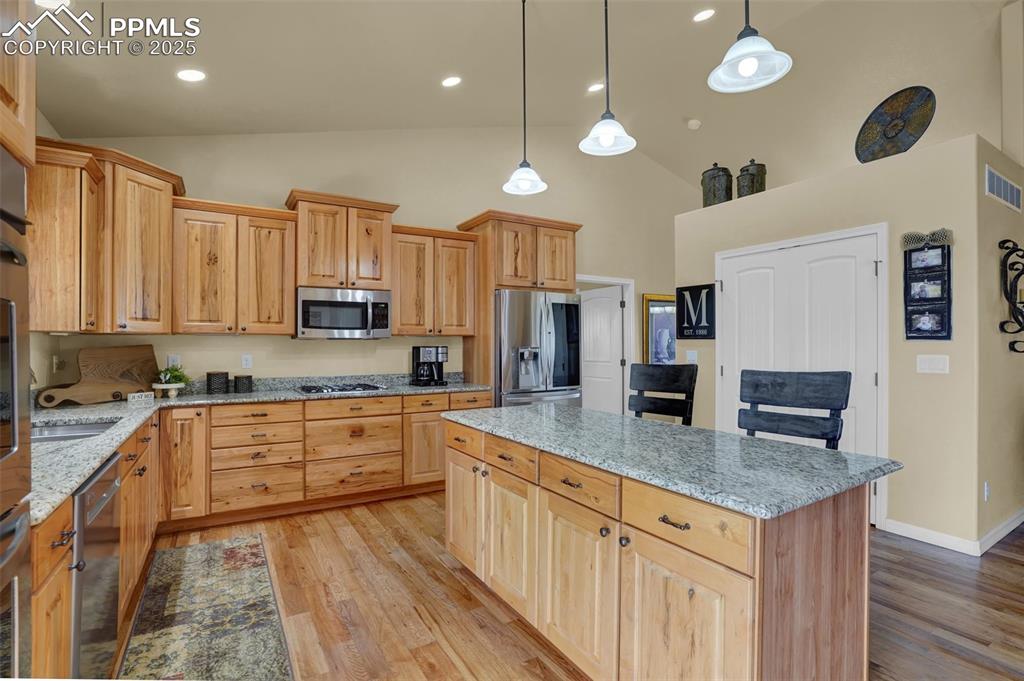 Kitchen with light wood finished floors, a kitchen island, light stone counters, decorative light fixtures, and stainless steel appliances