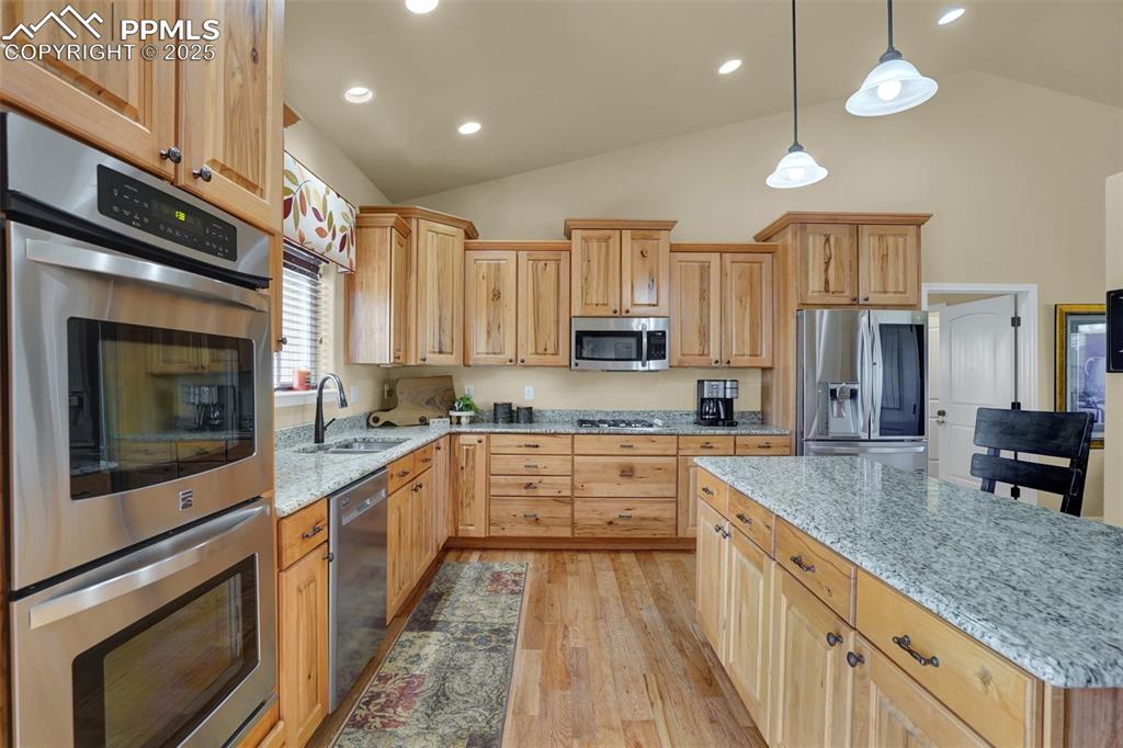 Kitchen with light stone counters, hanging light fixtures, stainless steel appliances, light wood-style floors, and a sink