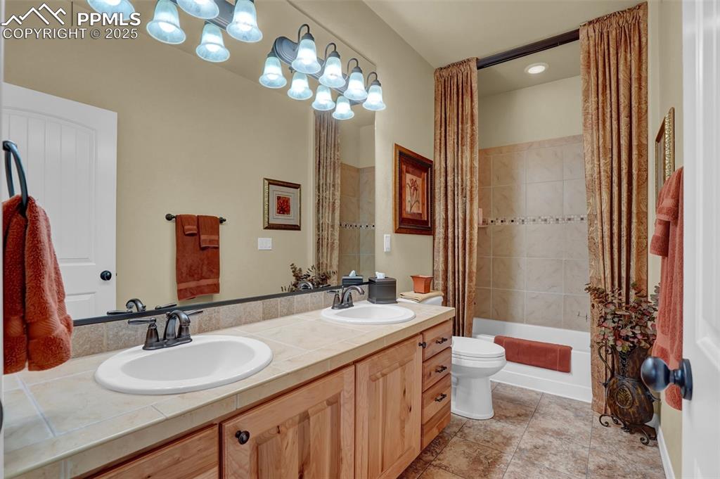 Bathroom featuring double vanity, shower / bath combination with curtain, a sink, and toilet