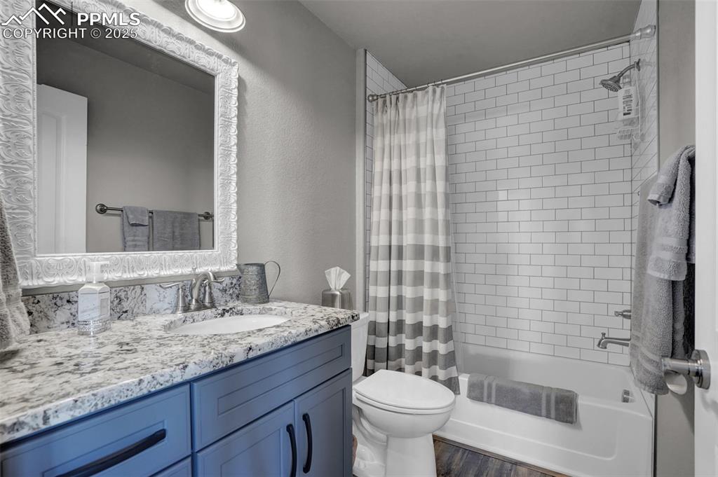 Bathroom featuring a textured wall, toilet, wood finished floors, vanity, and shower / bath combo
