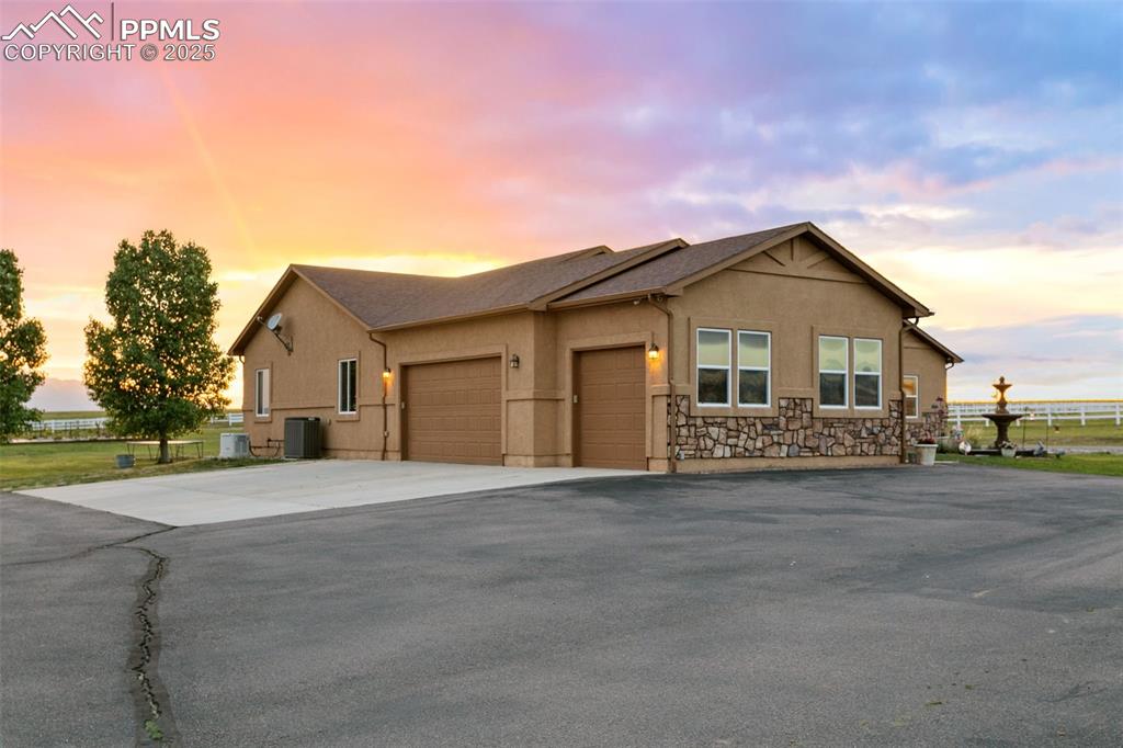 View of front of house with a garage, central AC, driveway, and stucco siding