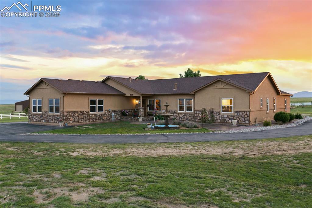 Front view of property featuring stone siding, a lawn, fence, and stucco siding