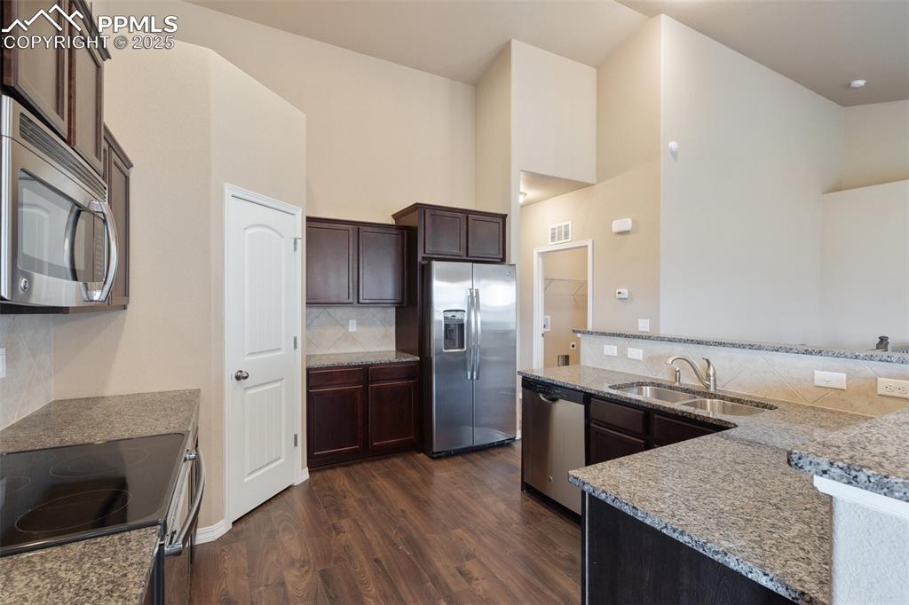 Kitchen featuring backsplash, dark wood-type flooring, appliances with stainless steel finishes, dark brown cabinetry, and light stone countertops