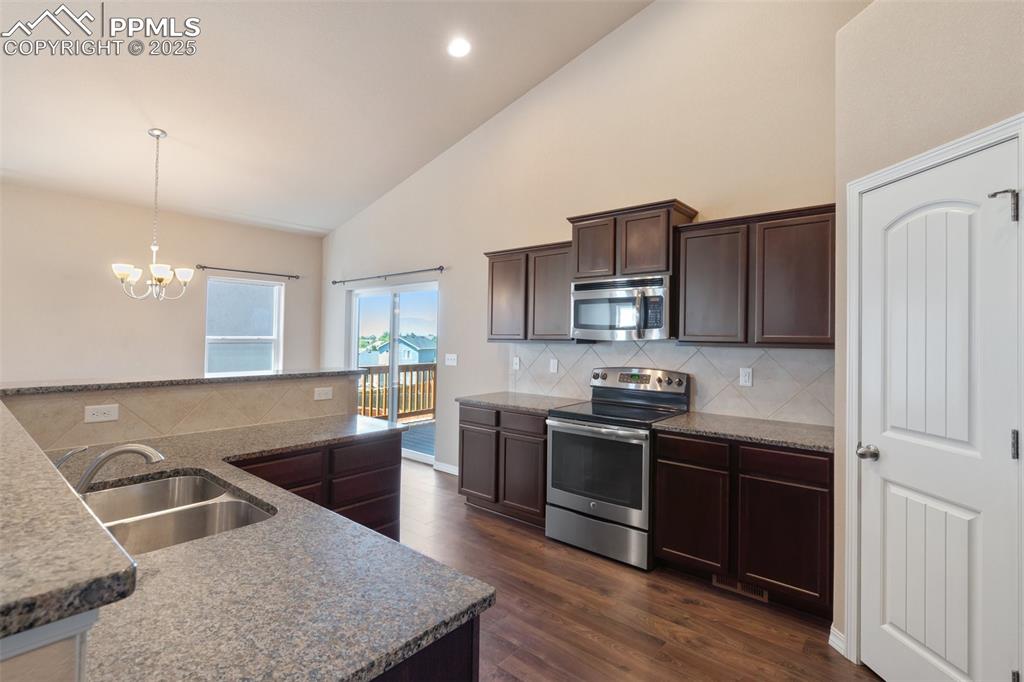 Kitchen with dark brown cabinets, appliances with stainless steel finishes, high vaulted ceiling, tasteful backsplash, and dark wood-style flooring