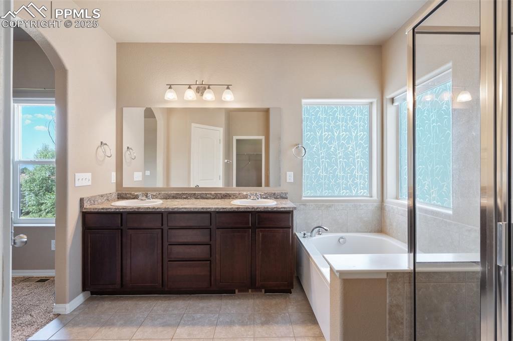 Bathroom featuring double vanity, a garden tub, light tile patterned floors, and a shower stall