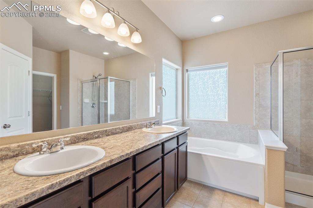 Bathroom with a shower stall, a walk in closet, double vanity, a bath, and recessed lighting