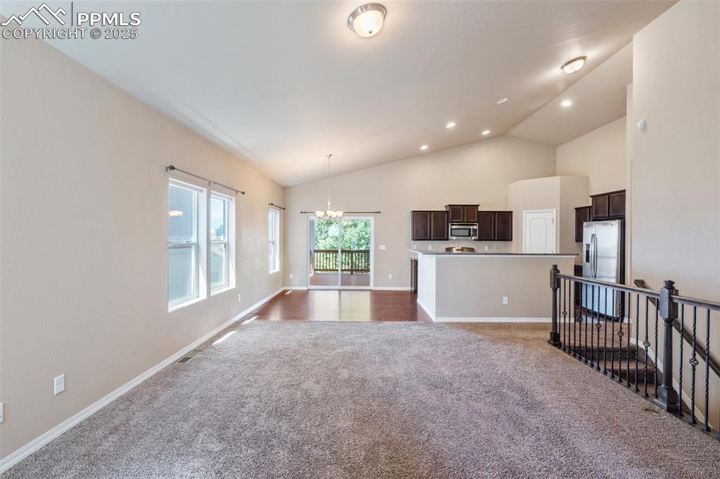 Unfurnished living room with dark carpet, a chandelier, high vaulted ceiling, and recessed lighting