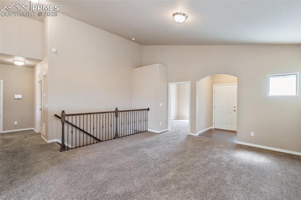 Spare room with carpet flooring, arched walkways, and high vaulted ceiling