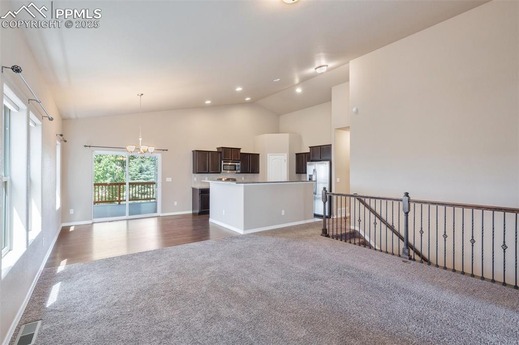 Unfurnished living room featuring a chandelier, dark carpet, high vaulted ceiling, recessed lighting, and dark wood-style flooring