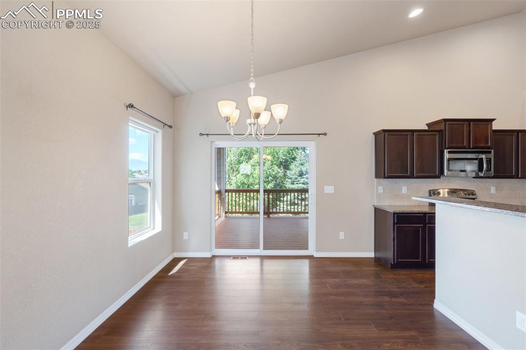 Kitchen with dark brown cabinets, lofted ceiling, a chandelier, light stone countertops, and stainless steel microwave