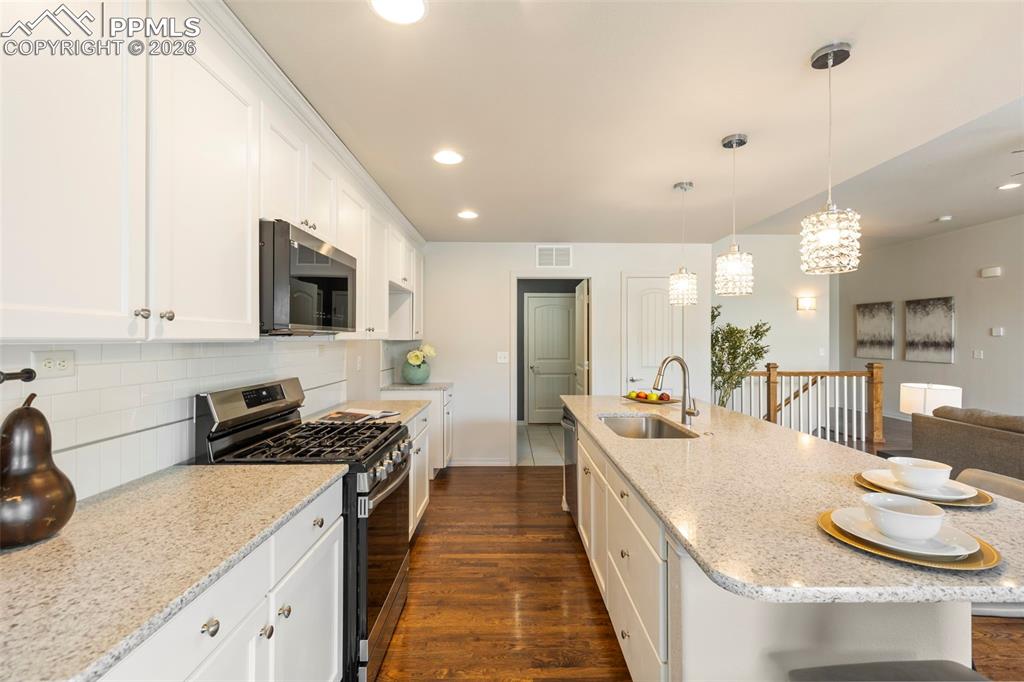 Kitchen with stainless steel appliances, light stone countertops, a kitchen breakfast bar, white cabinets, and dark wood-type flooring
