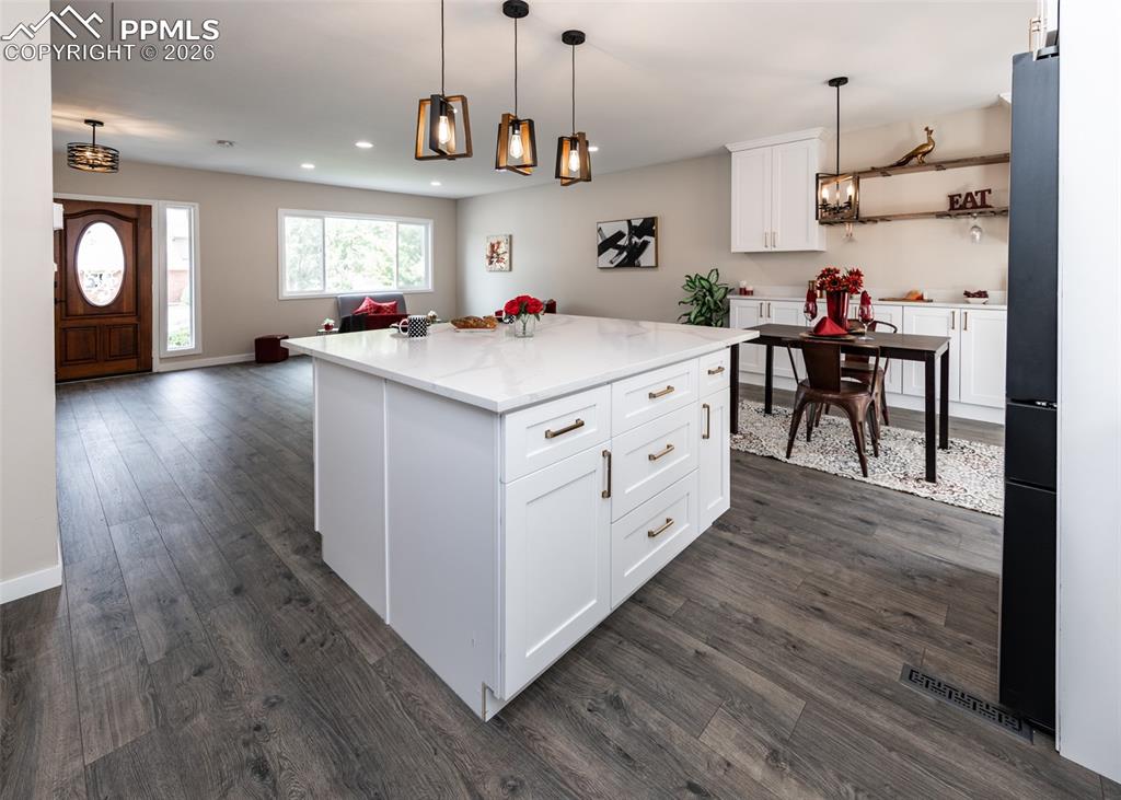 Kitchen with white cabinetry, pendant lighting, a center island, open floor plan, and light stone countertops