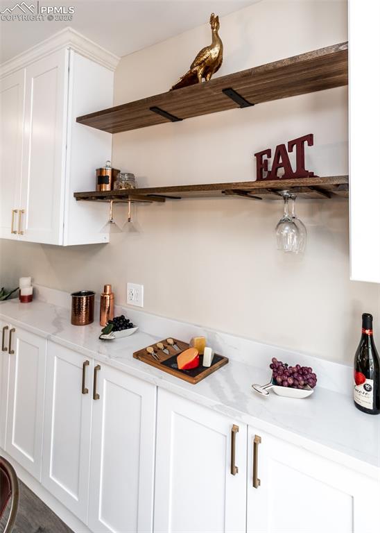 Bar with white cabinets, open shelves, and light stone countertops