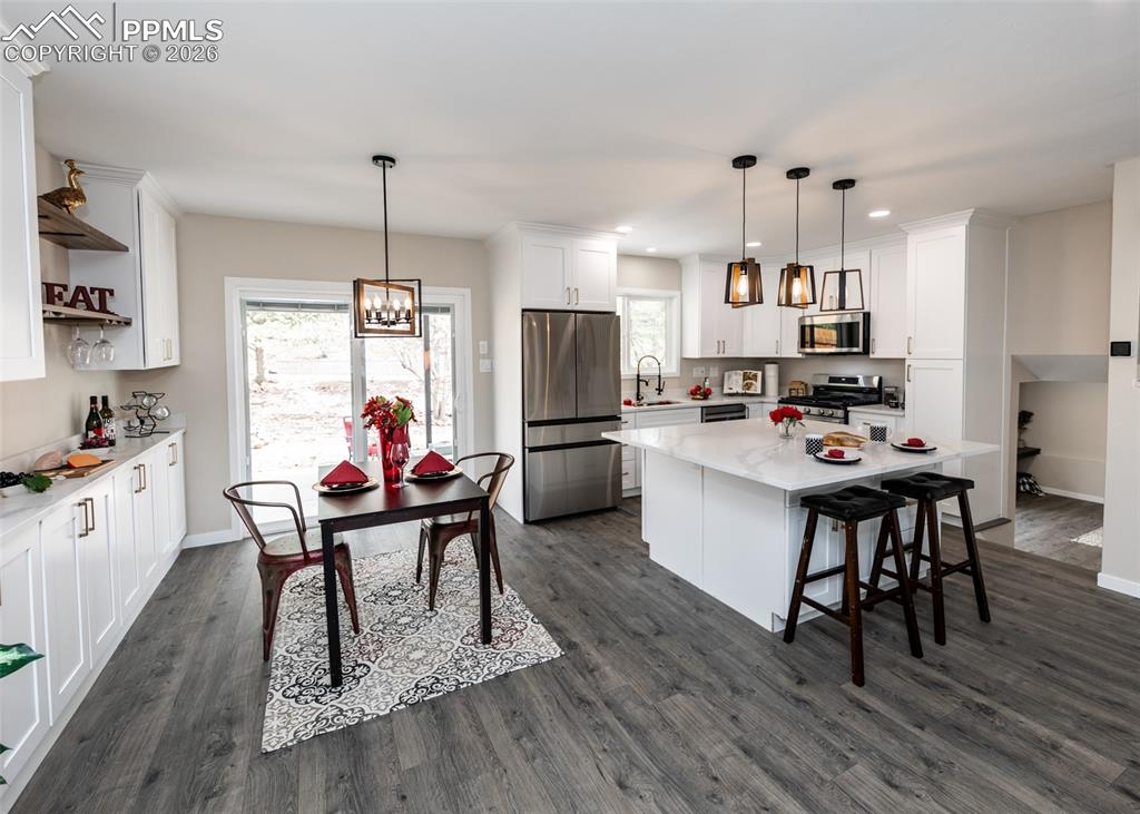 Kitchen featuring white cabinetry, appliances with stainless steel finishes, hanging light fixtures, a kitchen breakfast bar, and light stone counters