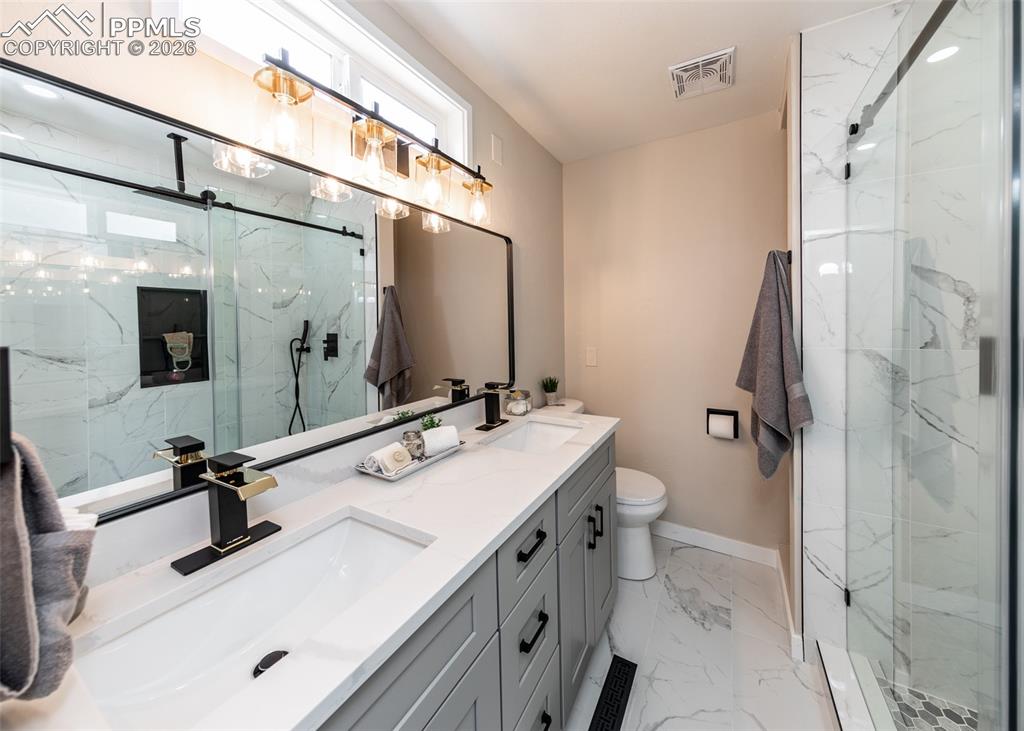 Bathroom featuring double vanity, a marble finish shower, and light marble finish flooring