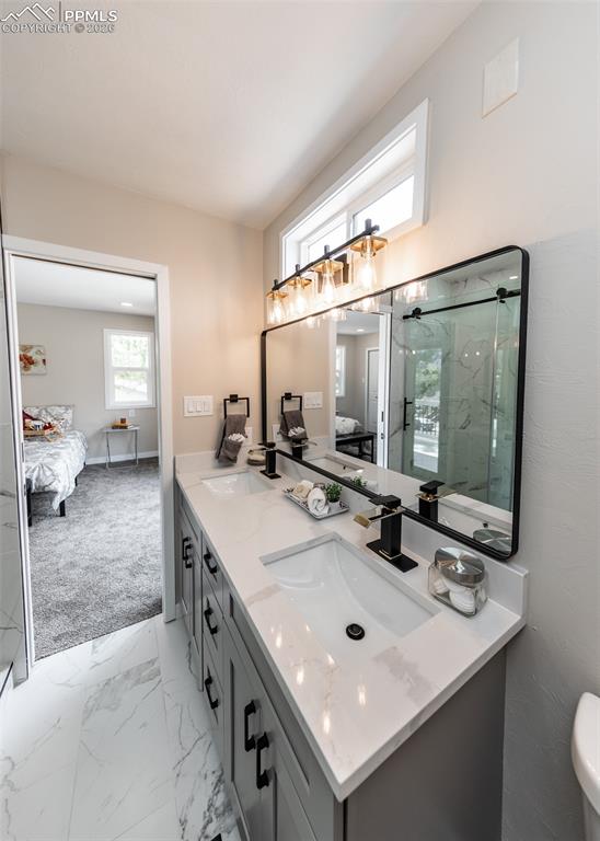 Ensuite bathroom with double vanity, light marble finish floors, and a marble finish shower