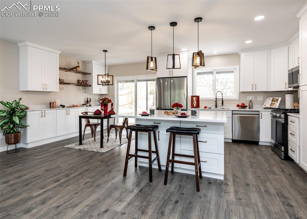 Kitchen featuring white cabinets, appliances with stainless steel finishes, a center island, hanging light fixtures, and plenty of natural light