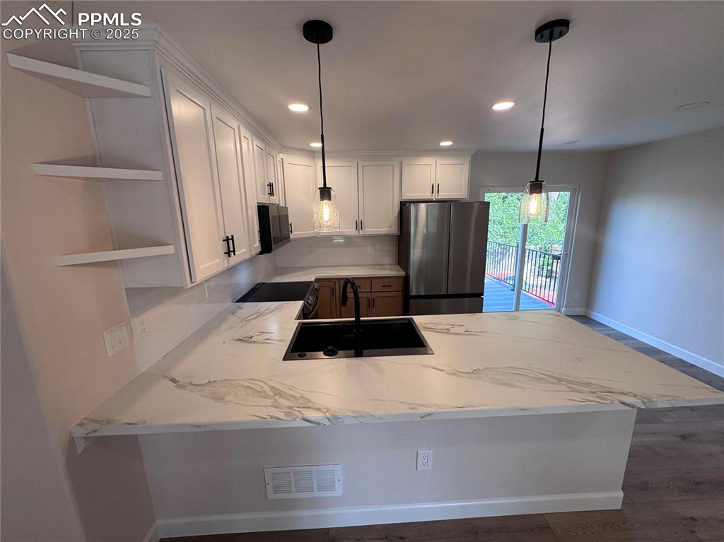 Kitchen featuring a peninsula, freestanding refrigerator, white cabinetry, hanging light fixtures, and tasteful backsplash