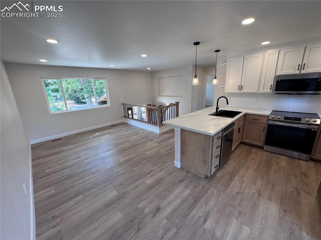 Kitchen with stainless steel appliances, white cabinetry, recessed lighting, a peninsula, and decorative light fixtures
