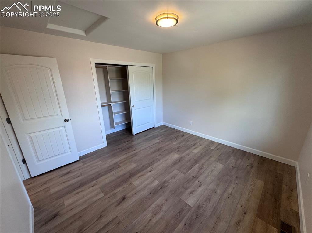 Unfurnished bedroom with attic access, wood finished floors, and a closet