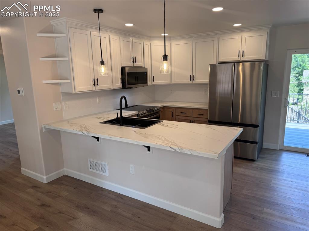 Kitchen featuring stainless steel appliances, pendant lighting, dark wood-type flooring, a peninsula, and recessed lighting