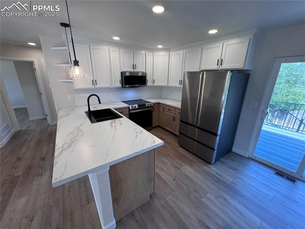 Kitchen with a peninsula, stainless steel appliances, recessed lighting, white cabinets, and hanging light fixtures