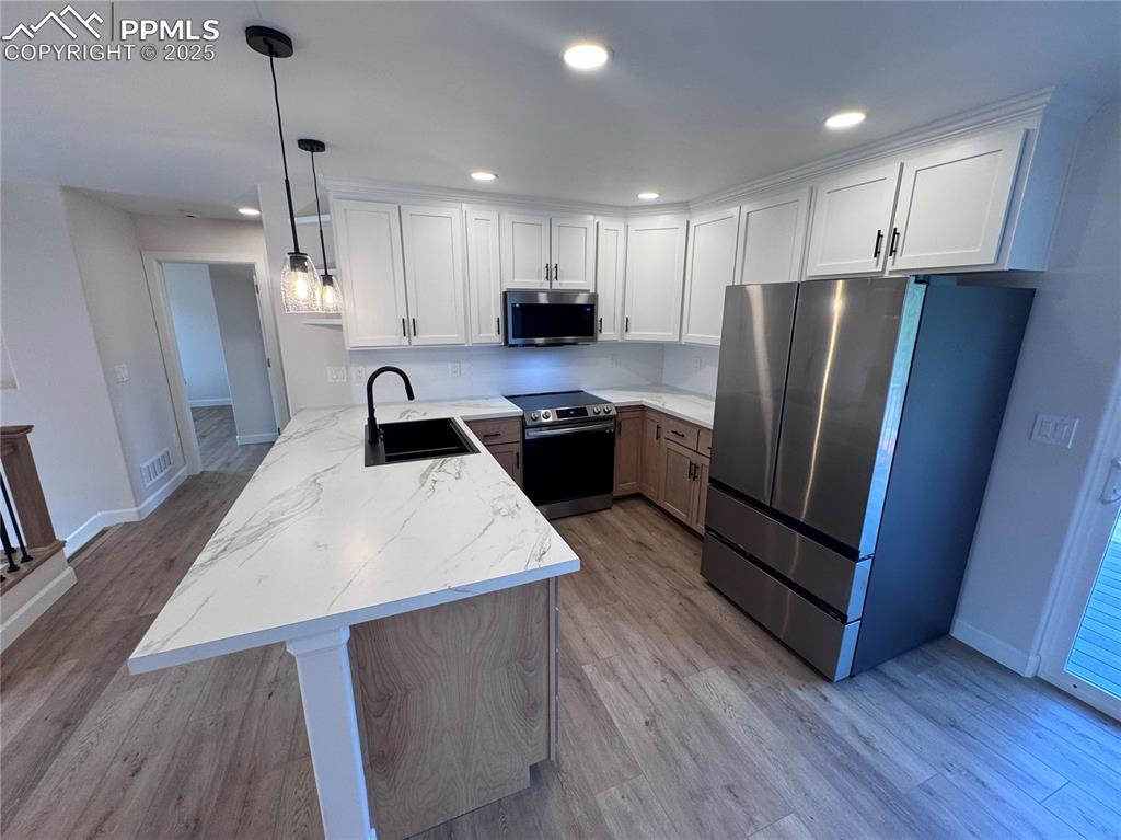 Kitchen with a peninsula, stainless steel appliances, recessed lighting, white cabinetry, and decorative light fixtures