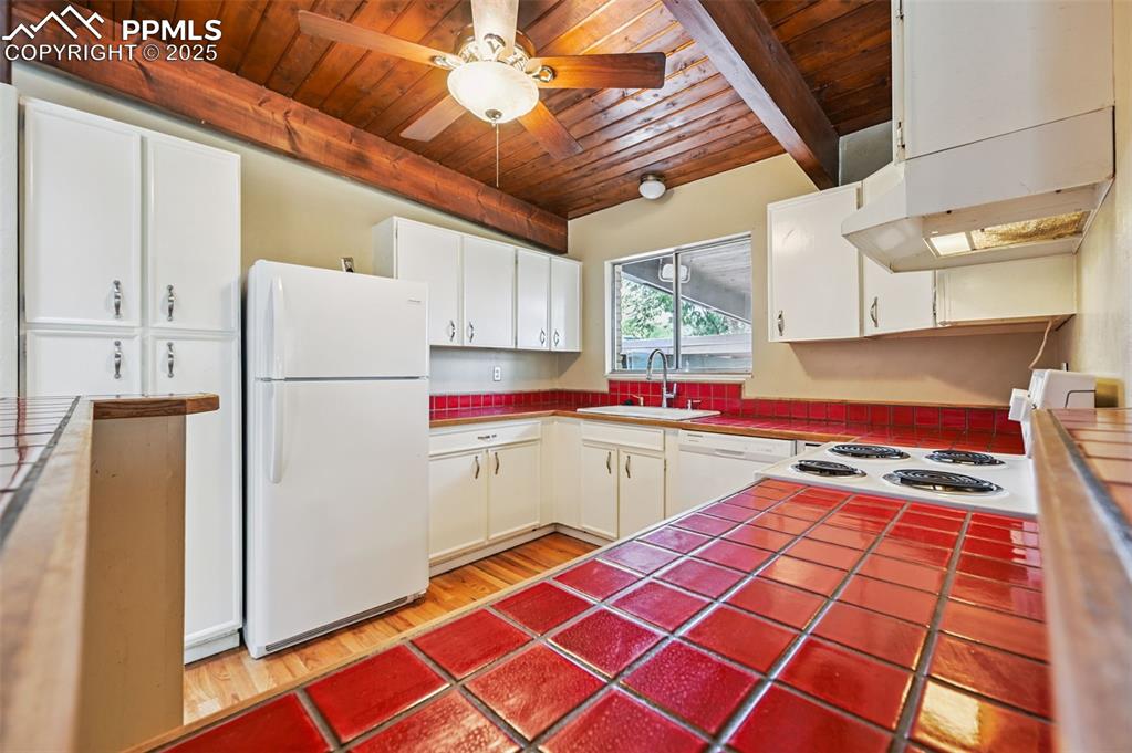 Kitchen w/ tile counters, a wood ceiling with exposed beams, white appliances, white cabinetry, and a ceiling fan