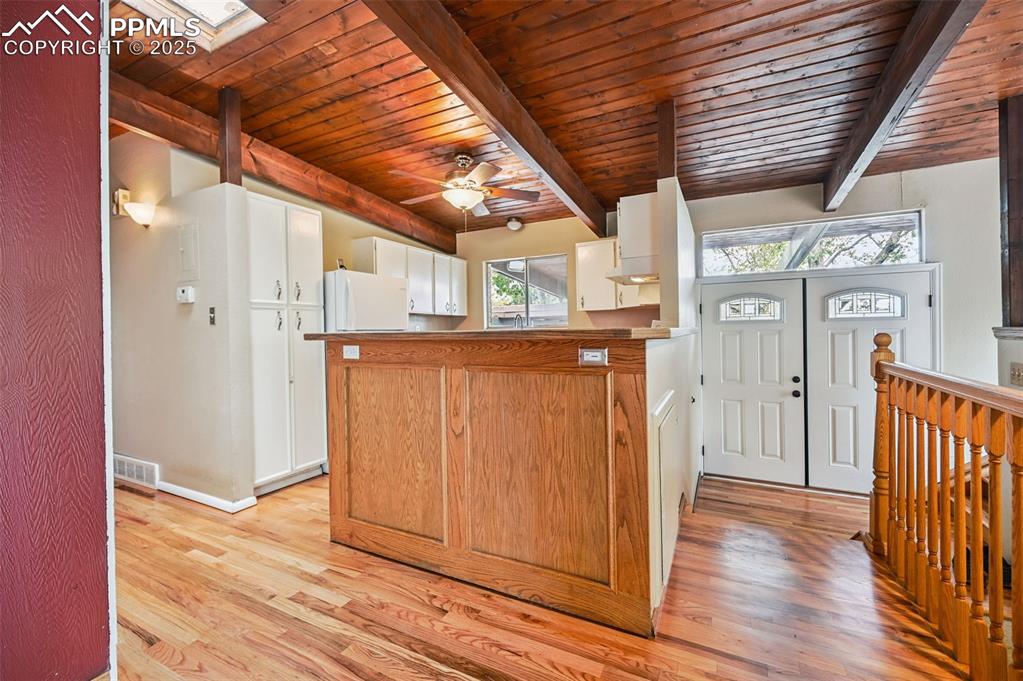 Kitchen featuring light wood finished floors, a wooden ceiling with exposed beams, a peninsula, a skylight, and a ceiling fan