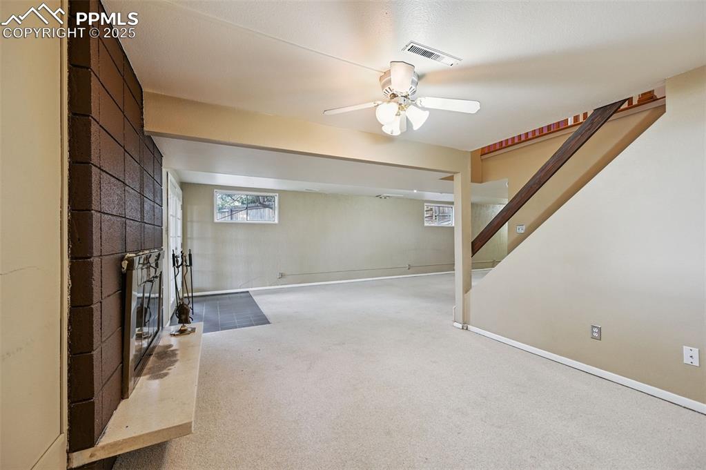 Basement featuring carpet flooring, stairway, ceiling fan, and a large fireplace