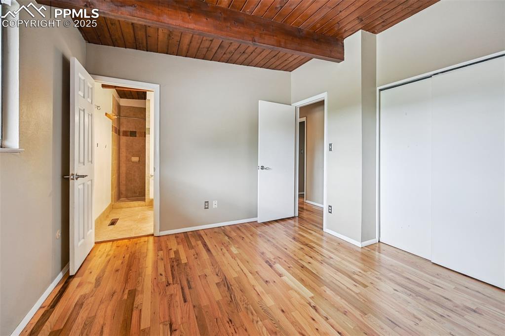 Unfurnished bedroom with a wooden ceiling with exposed beams, light wood-style floors, and a closet