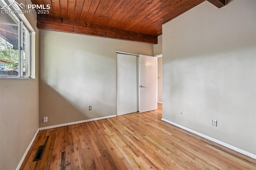 Unfurnished bedroom with a wood ceiling with exposed beams, wood finished floors, and a closet
