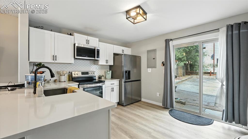 The bright kitchen features stylish laminate floors, crisp white cabinetry, solid-surface countertops, & a modern tile backsplash with slider to the back of the unit that includes parking and a storage unit.