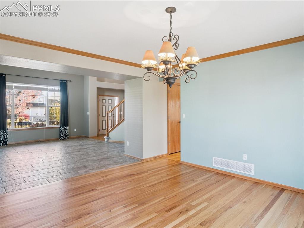 Unfurnished room with light wood-type flooring, crown molding, a chandelier, and stairway