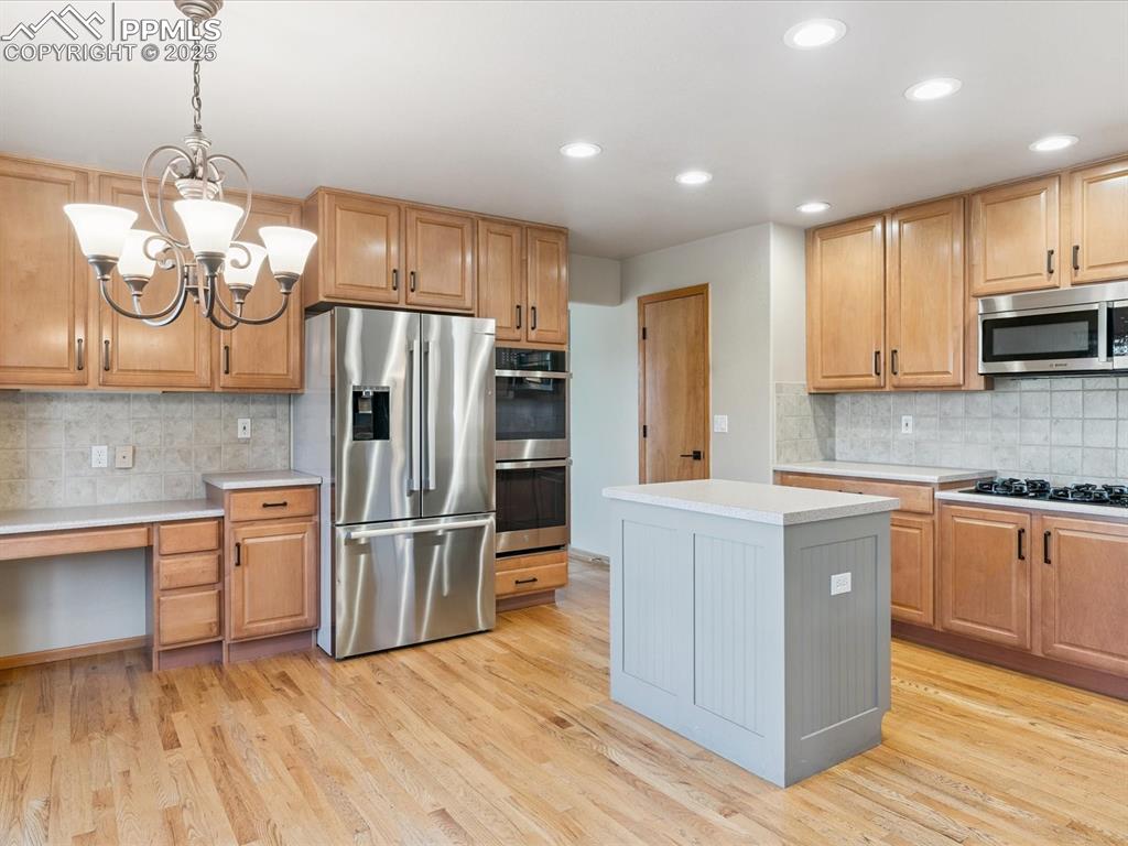Kitchen with backsplash, appliances with stainless steel finishes, light wood-style flooring, pendant lighting, and gray cabinets