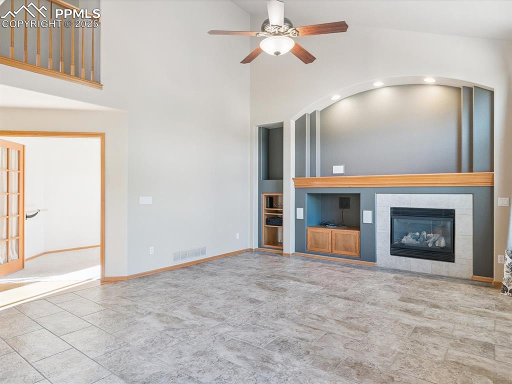 Unfurnished living room featuring built in features, a tiled fireplace, a ceiling fan, and high vaulted ceiling
