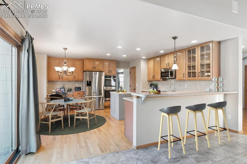 Virtually staged, kitchen with a breakfast bar, appliances with stainless steel finishes, a chandelier, light countertops, and a peninsula