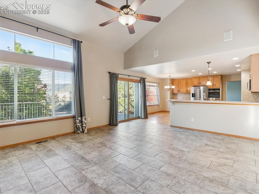 Unfurnished living room featuring a chandelier, high vaulted ceiling, and ceiling fan