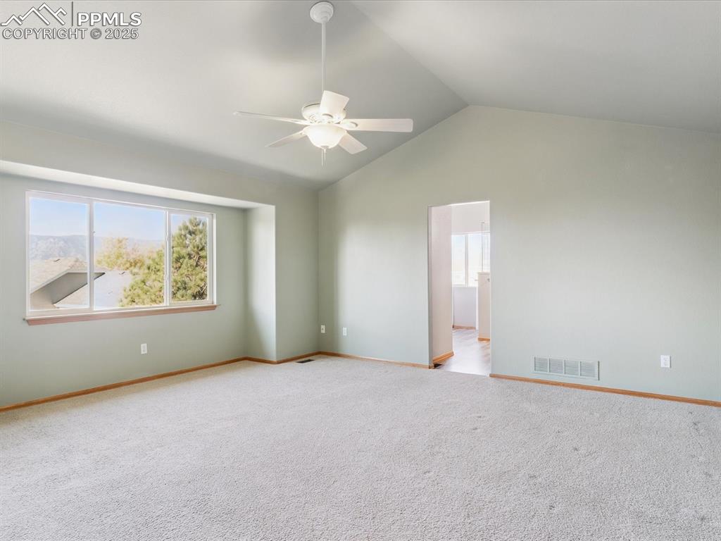 Empty room featuring vaulted ceiling, light colored carpet, and a ceiling fan