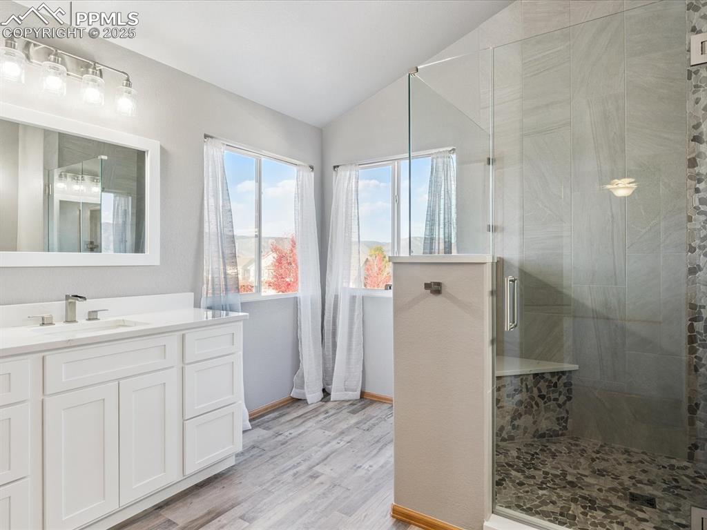 Bathroom featuring lofted ceiling, vanity, a shower stall, and light wood-style floors