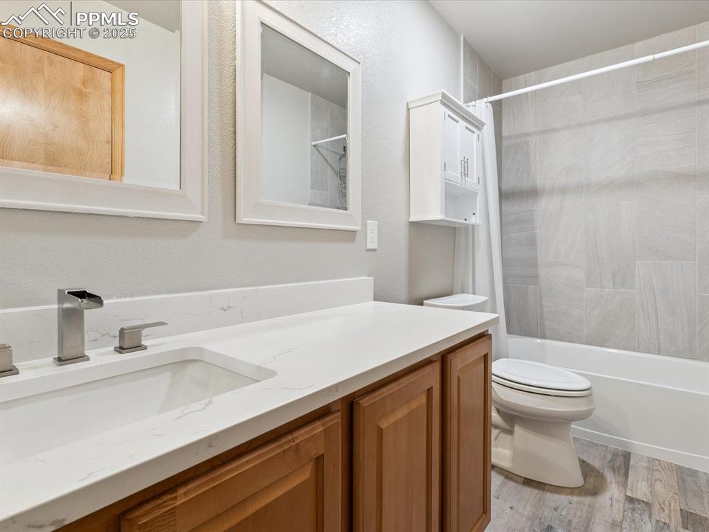Full bathroom with vanity, shower / bath combo with shower curtain, light wood-type flooring, and a textured wall