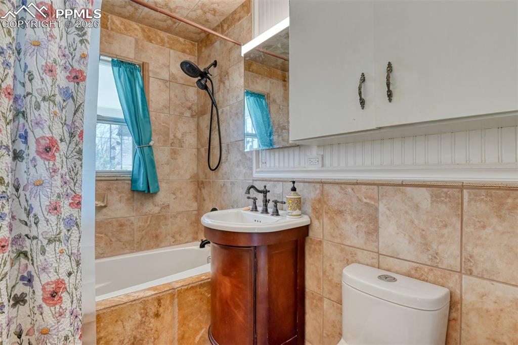 Full bathroom with toilet, tiled shower / bath combo, and tile walls