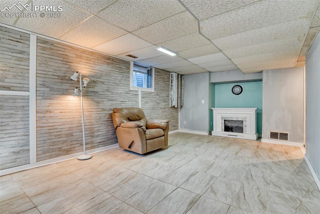 Unfurnished room featuring visible vents, baseboards, a drop ceiling, and a fireplace with raised hearth