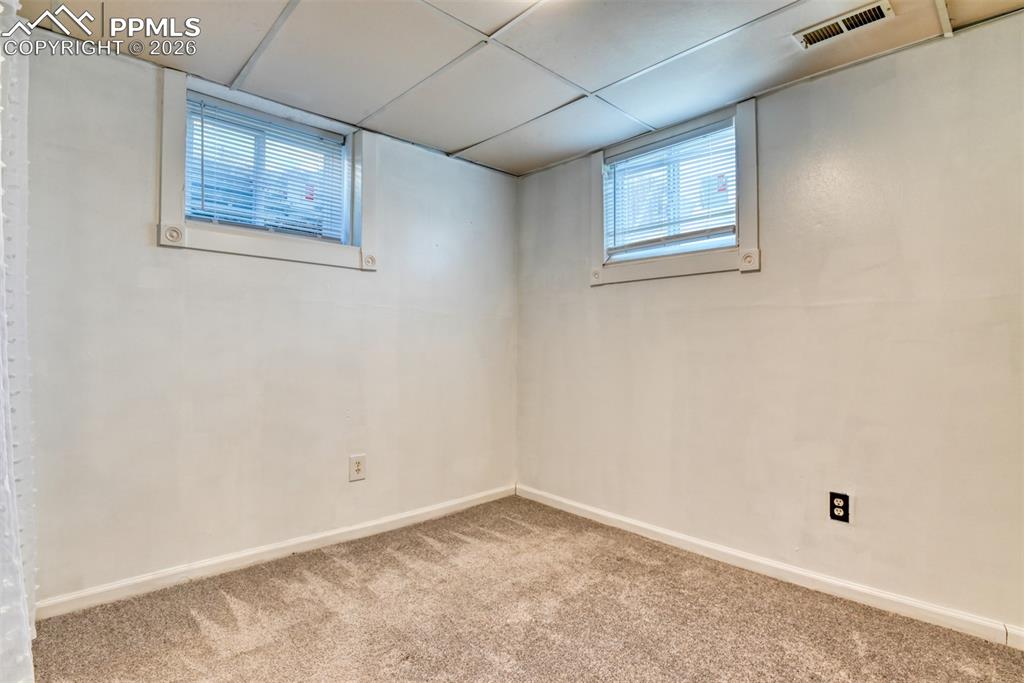 Basement featuring carpet flooring, visible vents, a drop ceiling, and baseboards